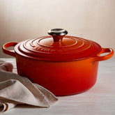 Panela laranja sobre superfície clara com pano de algodão ao lado. Design clássico e elegante, ideal para cozimentos lentos, assados e receitas sofisticadas com alta retenção de calor.